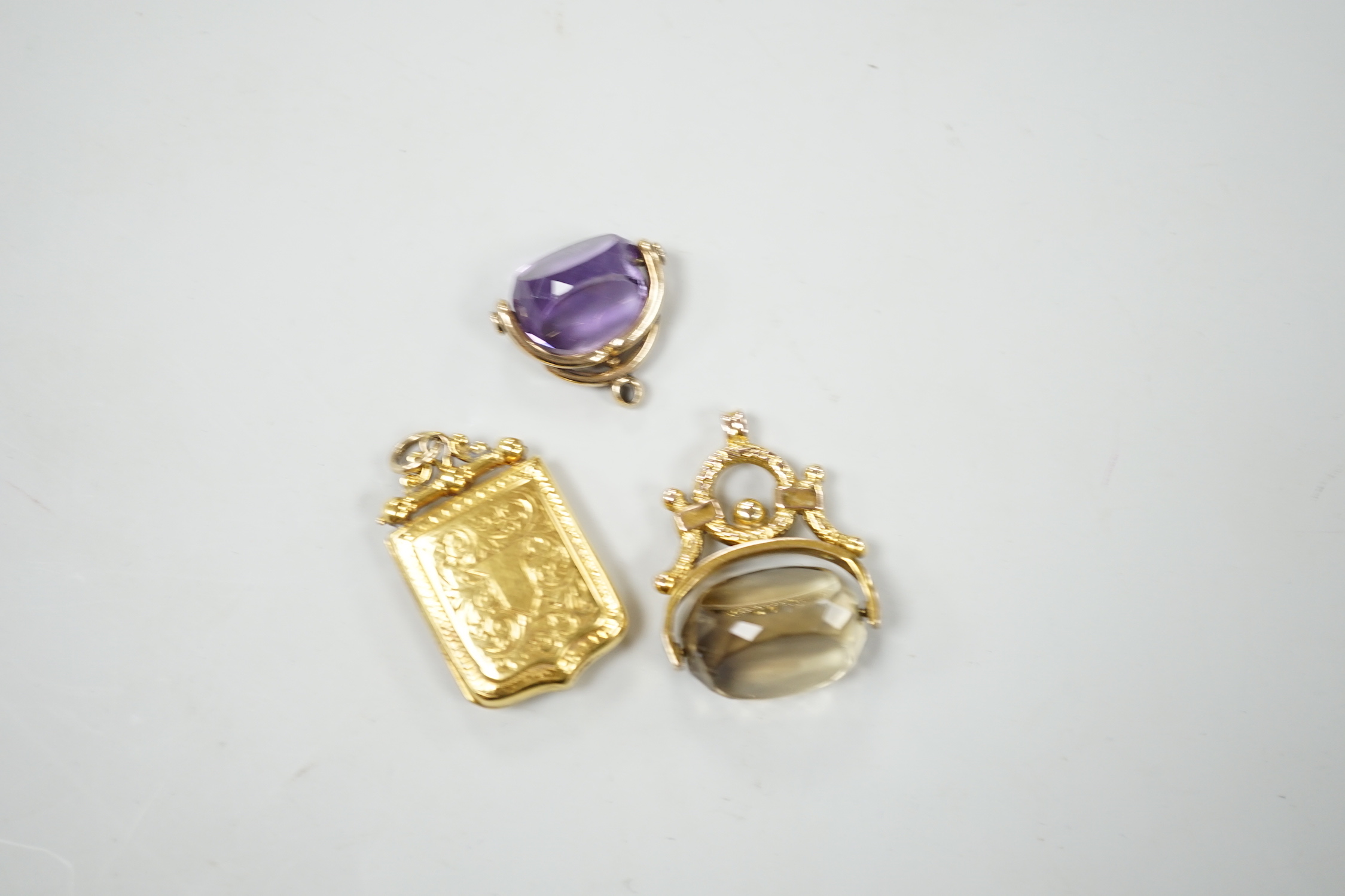 A Victorian engraved yellow metal shield shaped locket, 33mm and two yellow metal and gem set spinning fobs.